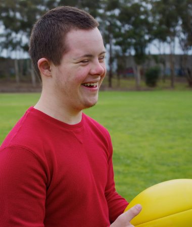 Sixteen-year-old boy smiling while holding football at park.