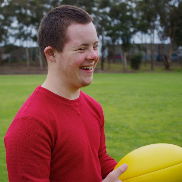 Sixteen-year-old boy smiling while holding football at park.